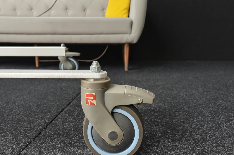 Front view of a simple home patient lift with wheeled base beside a comfy sofa – suitable for in-home care